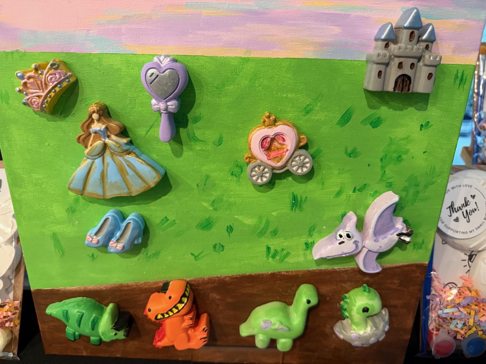 A display board of finished kits painted in bright colors: a princess, carriage, castle, crown, slippers and a row of dinosaurs